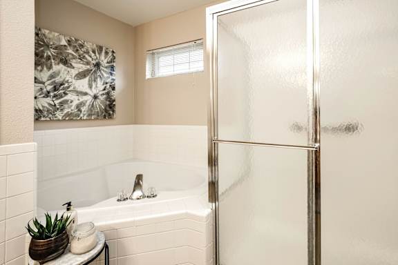 A bathroom with a white tub and a glass shower door. at Tranquility Pointe, Omaha, NE