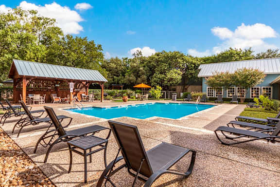 A pool area with lounge chairs and a pavilion.