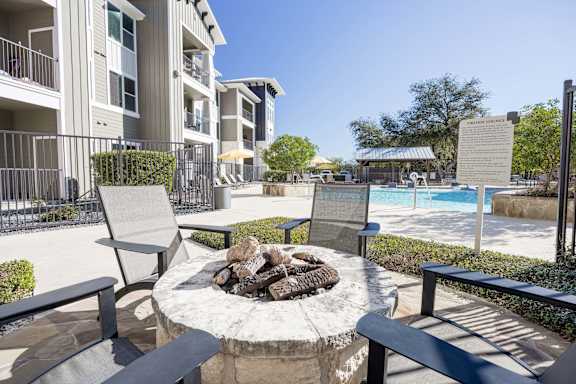 A fire pit sits in the middle of a patio surrounded by chairs.