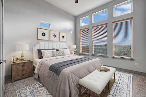 A bedroom with a large bed, a bench, and a window with blinds.