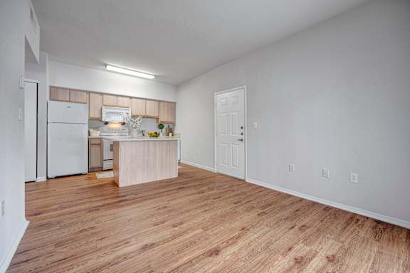 A kitchen with white appliances and wooden floors.