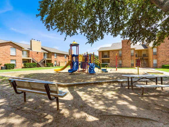 Community playground and picnic area with shaded seating at Quail Crossing Apartments, Grand Prairie, Texas