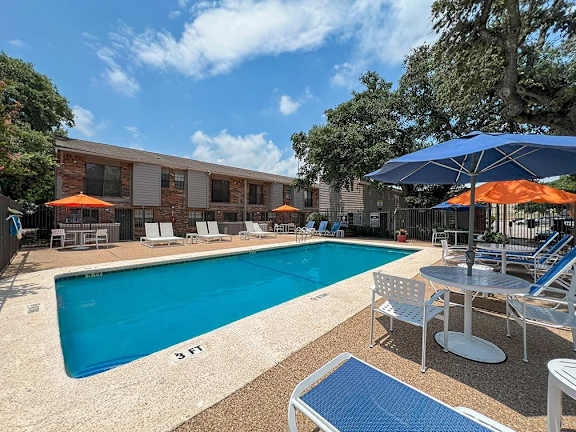 Swimming pool area with shade umbrellas and loungers at Autumn Chase Apartments, San Marcos, 78666