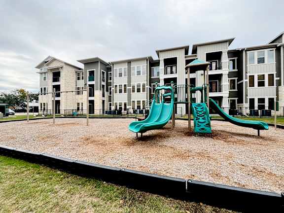 A playground with a green slide in front of apartment buildings.
