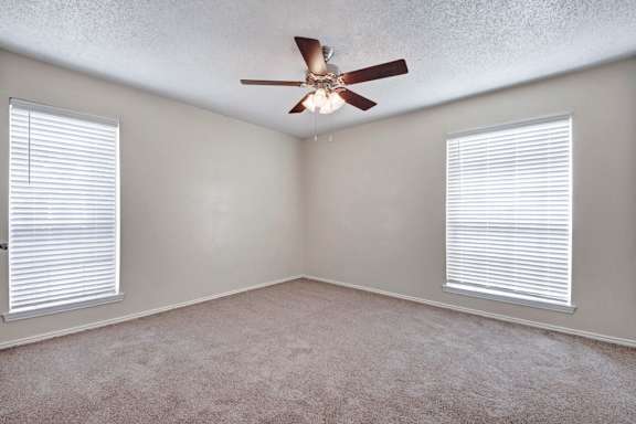 A room with a ceiling fan and two windows with blinds.