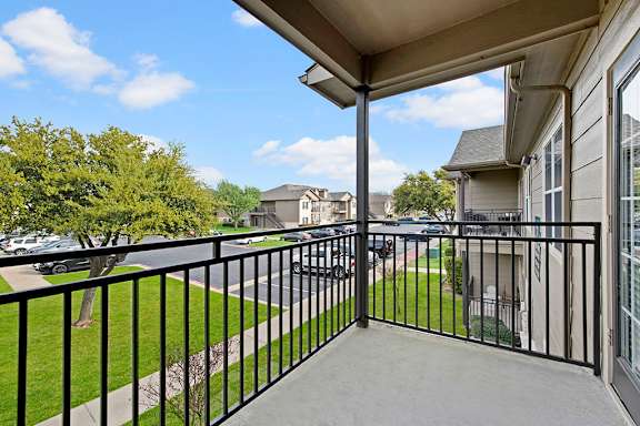 A balcony with a black railing overlooks a residential street.