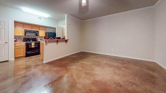 A large empty room with a kitchen area in the background.