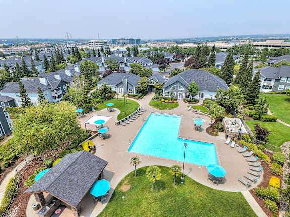 A large swimming pool surrounded by a grassy area and a trees.at Rosemeade Apartments, Roseville, California