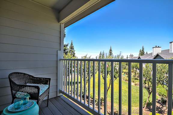 A chair and table are on a porch with a view of a green lawn and trees at Rosemeade Apartments, Roseville, 95661