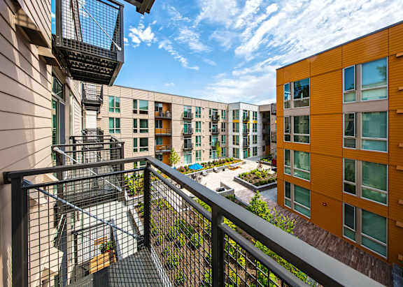 A balcony with a black railing overlooks a courtyard with a fountain and seating area.