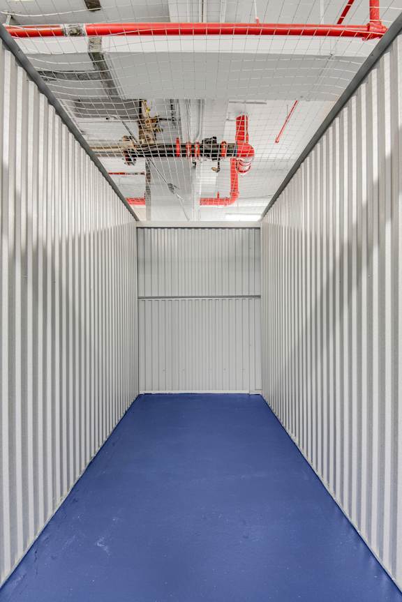 A long hallway with a blue floor and white walls with red pipes.