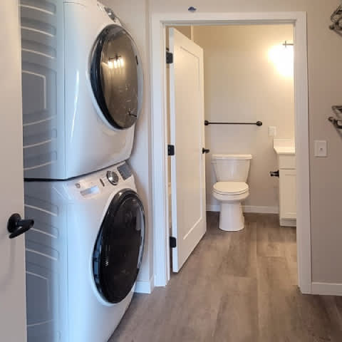 A white washing machine is in a laundry room with a toilet in the background.