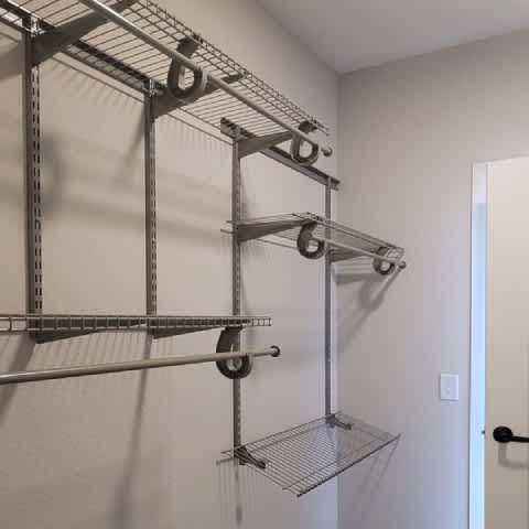 A metal shelving unit with four shelves is mounted on a white wall.