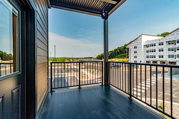 A balcony with a black railing and a view of a parking lot and a building.
