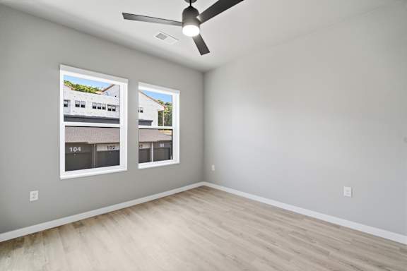 A room with a ceiling fan and two windows showing the exterior of a building.
