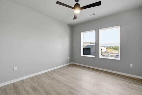 A room with a ceiling fan and two windows.