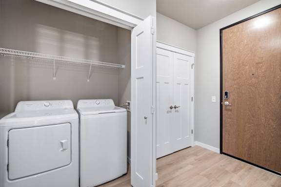 A laundry room with a white washer and dryer, a white closet, and a wooden door.