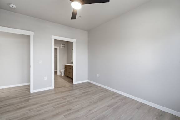 A room with a ceiling fan and light, and a doorway leading to another room.
