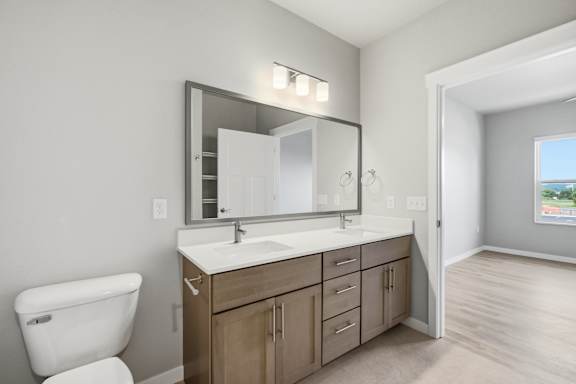 A bathroom with a white toilet, a sink with a mirror above it, and wooden cabinets.