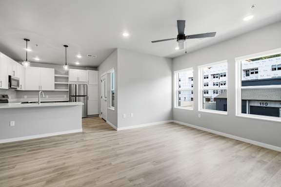 A spacious kitchen and living room with a ceiling fan and hardwood floors.