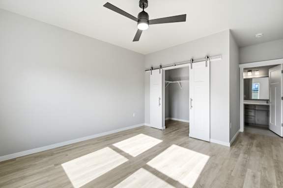 A room with a ceiling fan and sliding doors leading to another room.