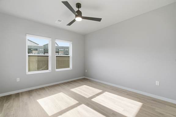 A room with a ceiling fan and two windows.