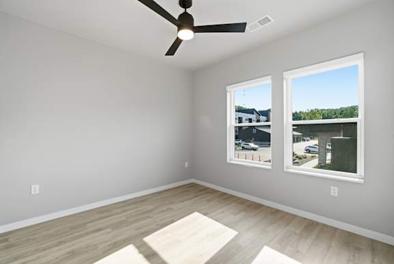 A room with a ceiling fan and two windows.