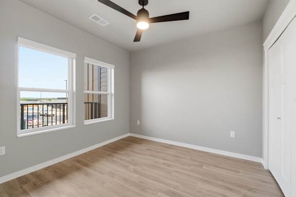 A room with a ceiling fan and two windows.