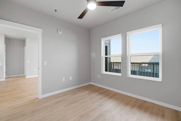 A room with a ceiling fan and two windows.