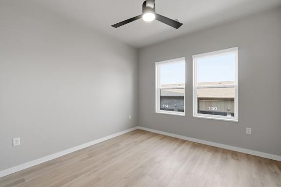 A room with a ceiling fan and two windows.