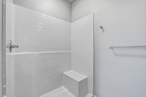 A white bathroom with a walk in shower and a white bench.