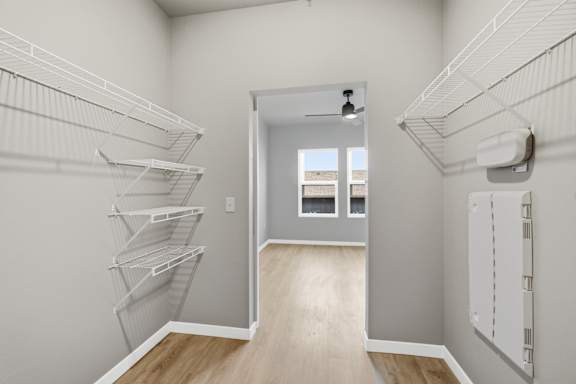A walk in closet with white shelves and a doorway leading to a hallway.