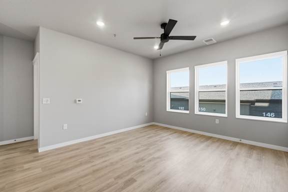 A spacious room with a ceiling fan and three windows.