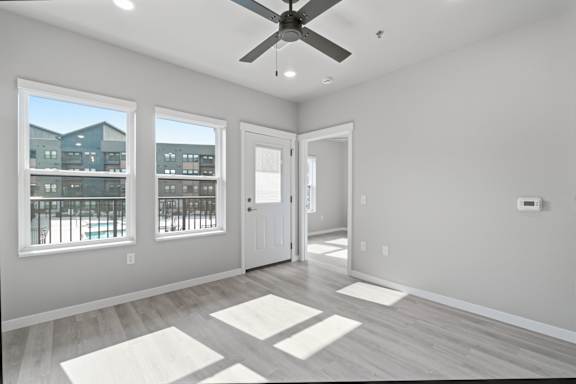 A room with a ceiling fan and a view of a building outside the window.