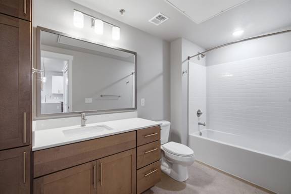 A bathroom with a sink, mirror, toilet and bathtub.