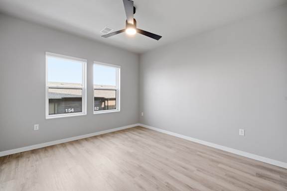 A room with a ceiling fan and two windows.