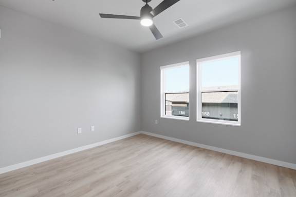 A room with a ceiling fan and two windows.