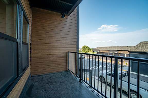 A balcony with a black railing and a white car parked in the background.