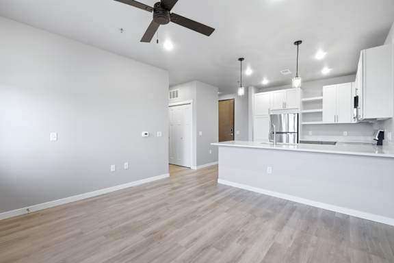 A spacious kitchen and living room with a ceiling fan and pendant lights.