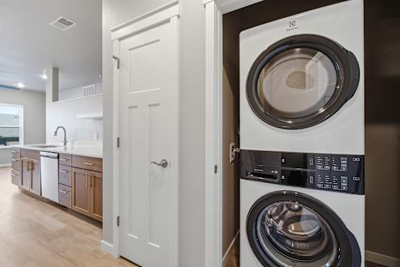 A white door is open to a modern laundry room with a washer and dryer.