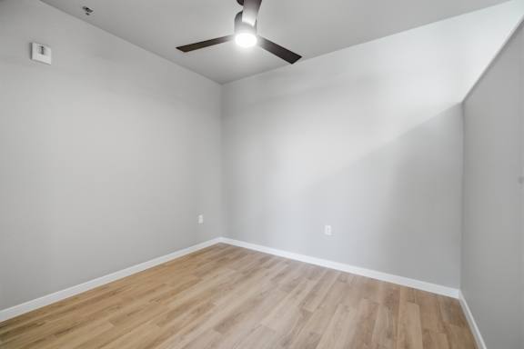 A room with a ceiling fan and wooden flooring.