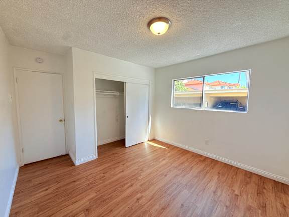 A room with wooden floors and a window showing a house.
