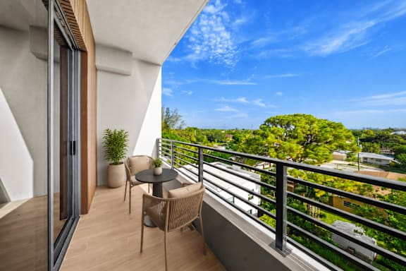 A balcony with a table and chairs overlooking a tree-filled landscape.