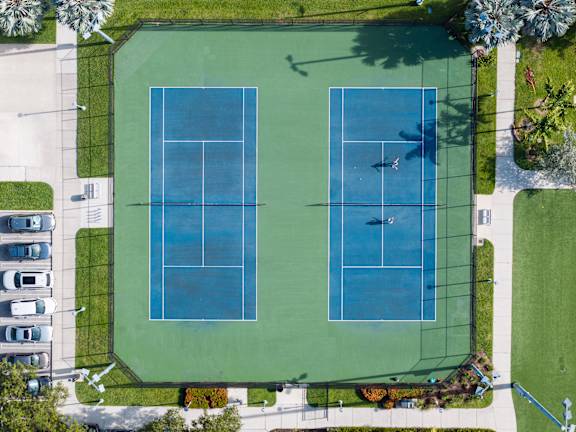 Two tennis courts surrounded by a green fence.