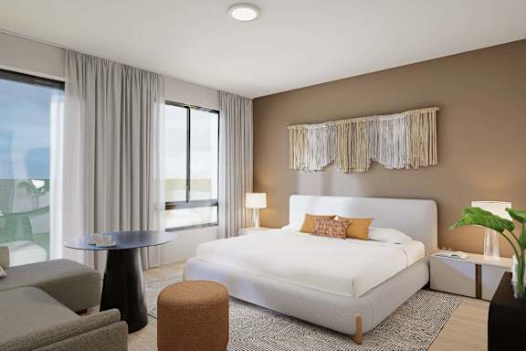 A modern bedroom with a large bed, a grey sofa, and a round table.