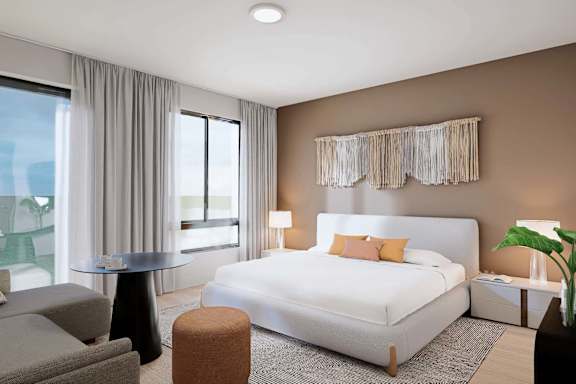 A modern bedroom with a large bed, a round table, and a window with curtains.