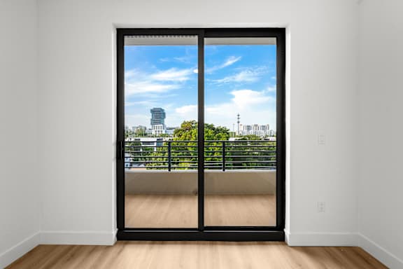 A room with a sliding door leading to a balcony with a view of the city.