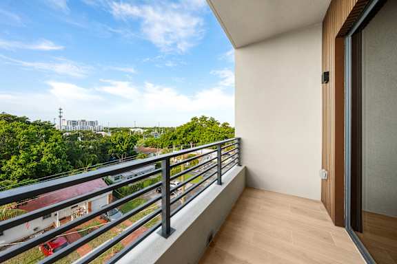 A balcony with a metal railing and a glass door overlooks a residential area.