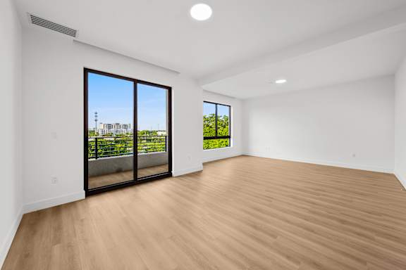 A room with a wooden floor and a view of a balcony with greenery.