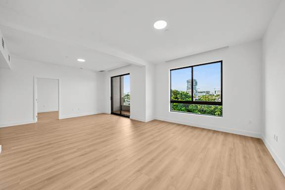 A large empty room with wooden floors and a view of a building outside the window.